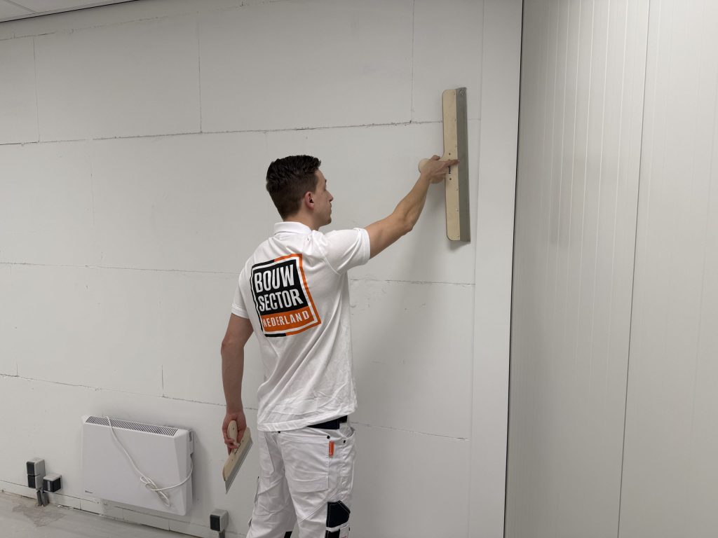 Stukadoor trekt een wand van gipsblokken vlak met een spaan, naast een lichte systeemwand