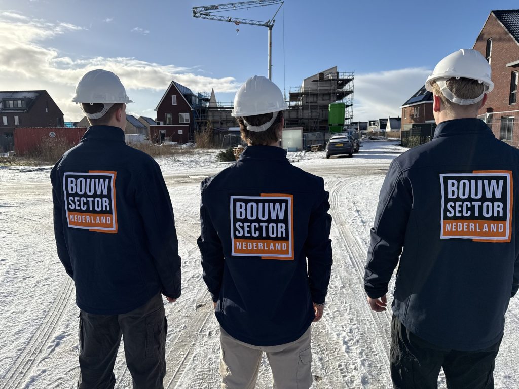 Drie vakmensen van Bouwsector Nederland met witte helm op een besneeuwd bouwterrein met woningen in aanbouw